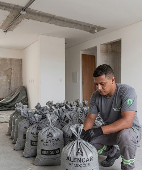 Profissional amarrando saco cinza de entulho ensacado da Alencar Remoções no interior de um apartamento em reforma.